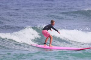 Young surfer riding a small ocean wave on a pink surfboard during a kids surfing experience on the North Shore of Oahu, Hawaii.