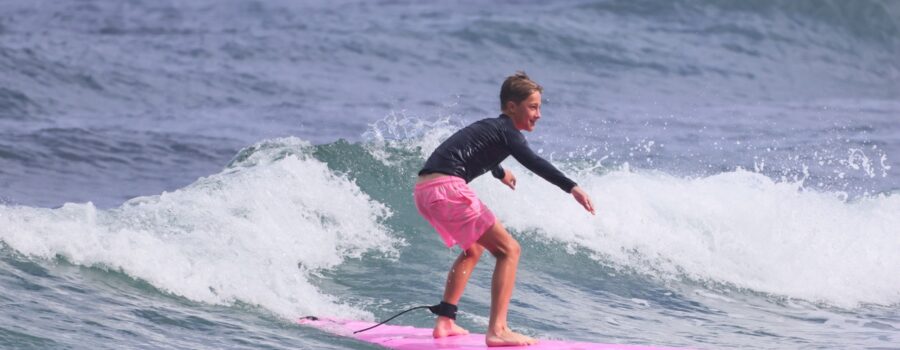 Young surfer riding a small ocean wave on a pink surfboard during a kids surfing experience on the North Shore of Oahu, Hawaii.
