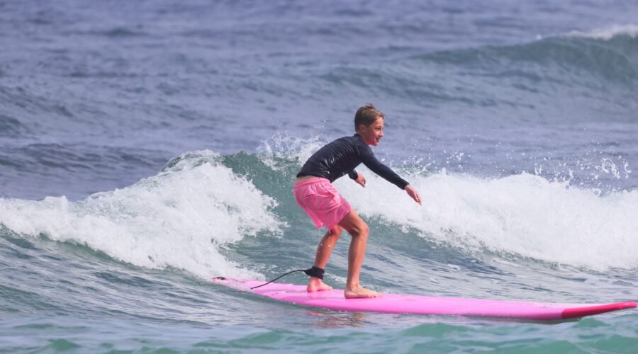 Young surfer riding a small ocean wave on a pink surfboard during a kids surfing experience on the North Shore of Oahu, Hawaii.