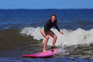 Woman surfing a breaking wave on a pink longboard during a North Shore Oahu surf lesson.