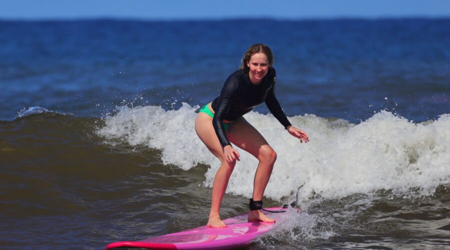 Woman surfing a breaking wave on a pink longboard during a North Shore Oahu surf lesson.