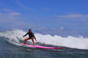 Woman surfing a Hawaiian wave on a bright pink longboard, representing North Shore Oahu surf lessons.