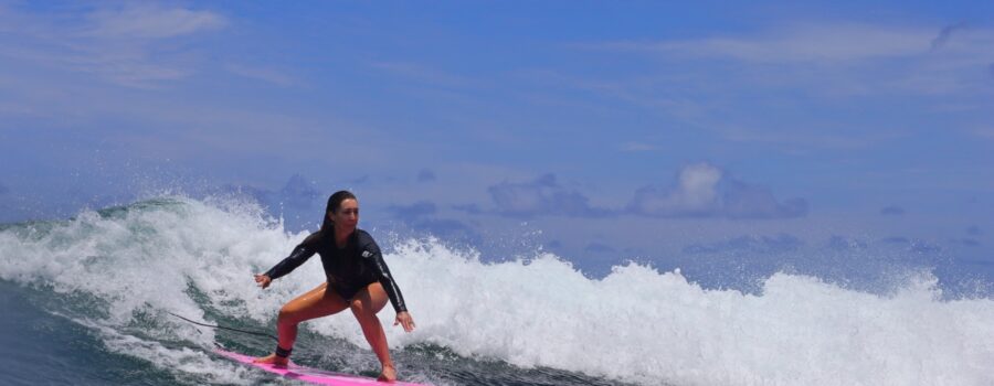Woman surfing a Hawaiian wave on a bright pink longboard, representing North Shore Oahu surf lessons.