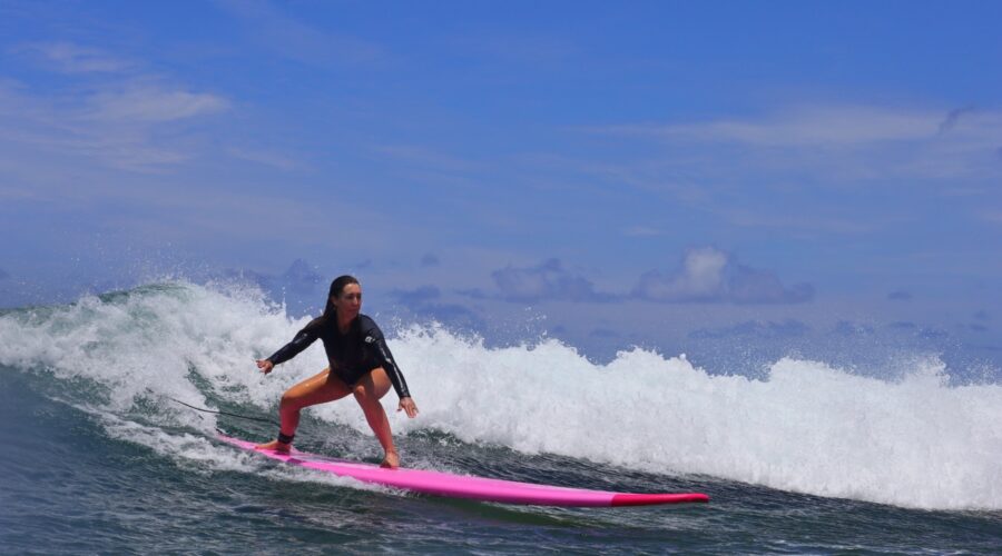 Woman surfing a Hawaiian wave on a bright pink longboard, representing North Shore Oahu surf lessons.